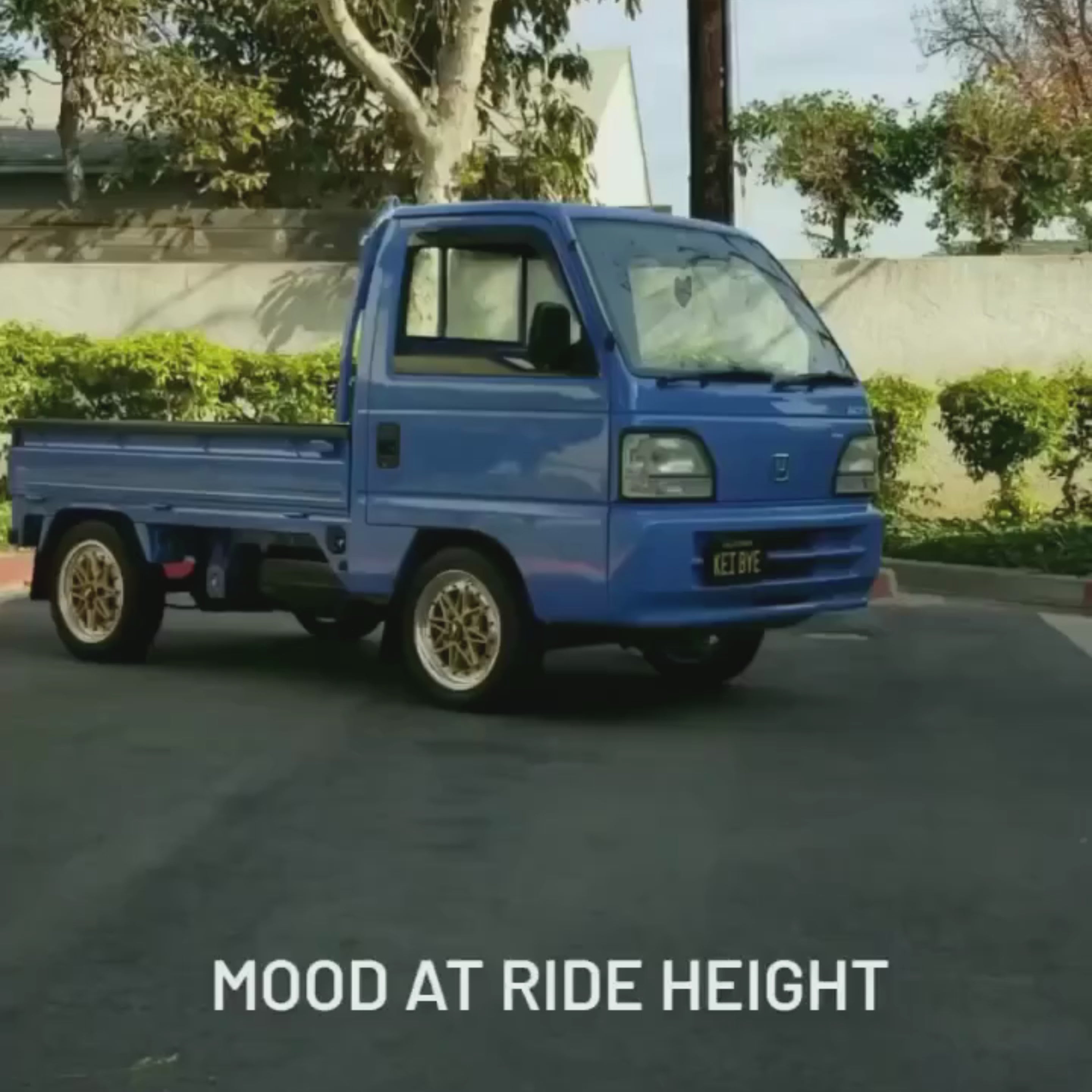 Customized Honda Acty truck with blue body and lowered air suspension, showcasing sleek aftermarket wheels in a garage setting